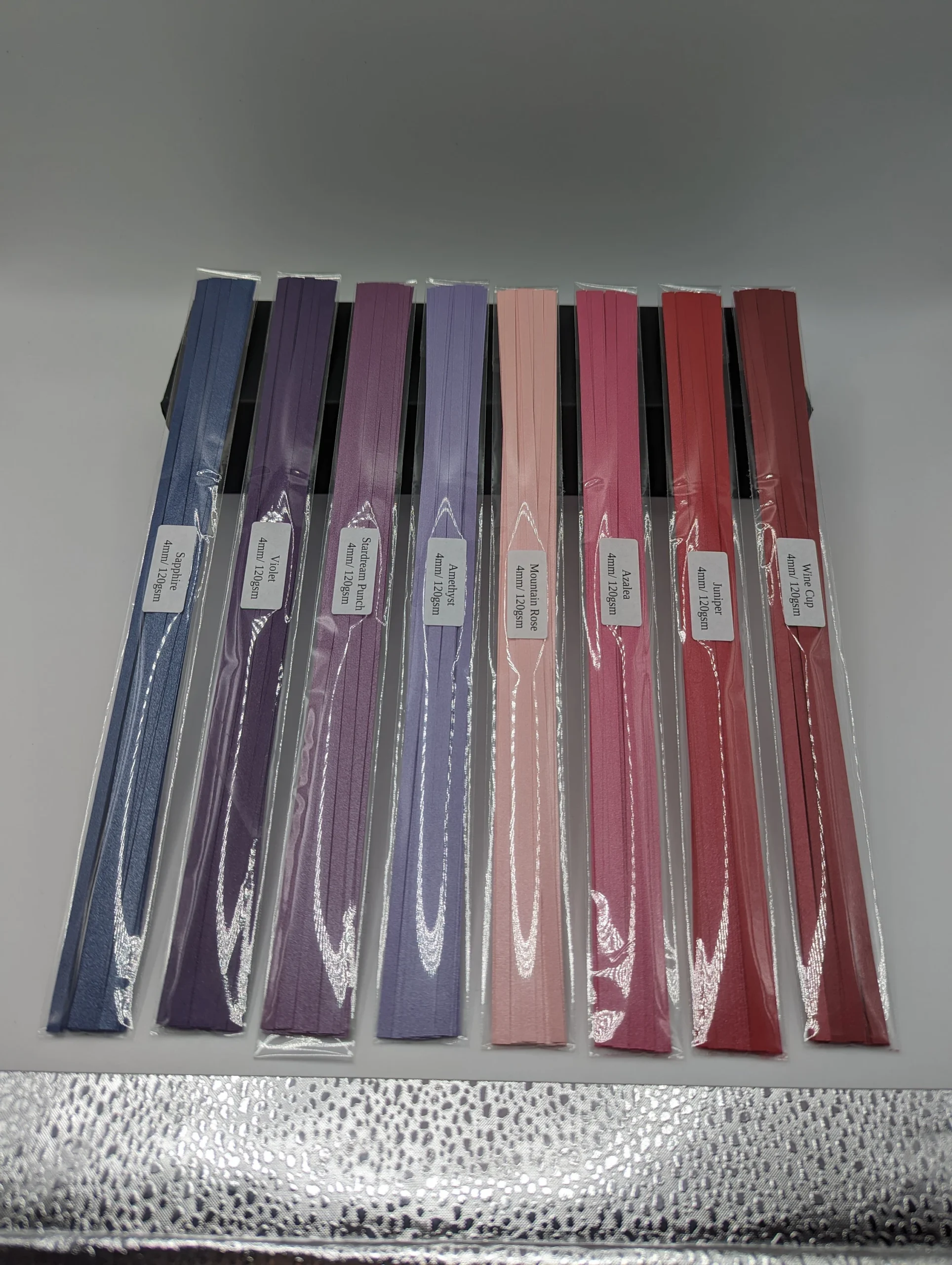 Assorted colorful strips of midweight 120 GSM quilling paper with matte and pearl finishes displayed in a fan arrangement on white background