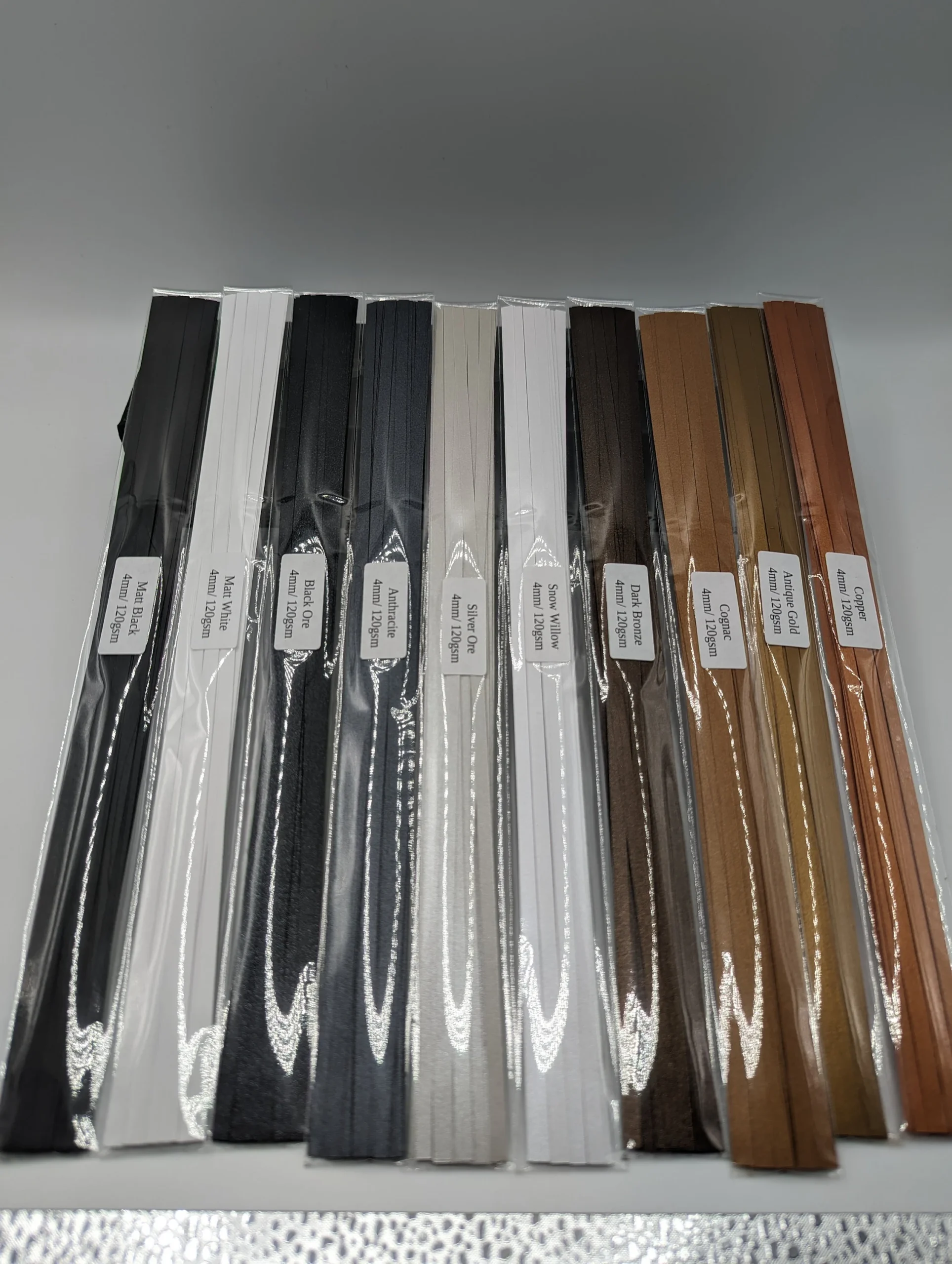 Assorted colorful strips of midweight 120 GSM quilling paper with matte and pearl finishes displayed in a fan arrangement on white background